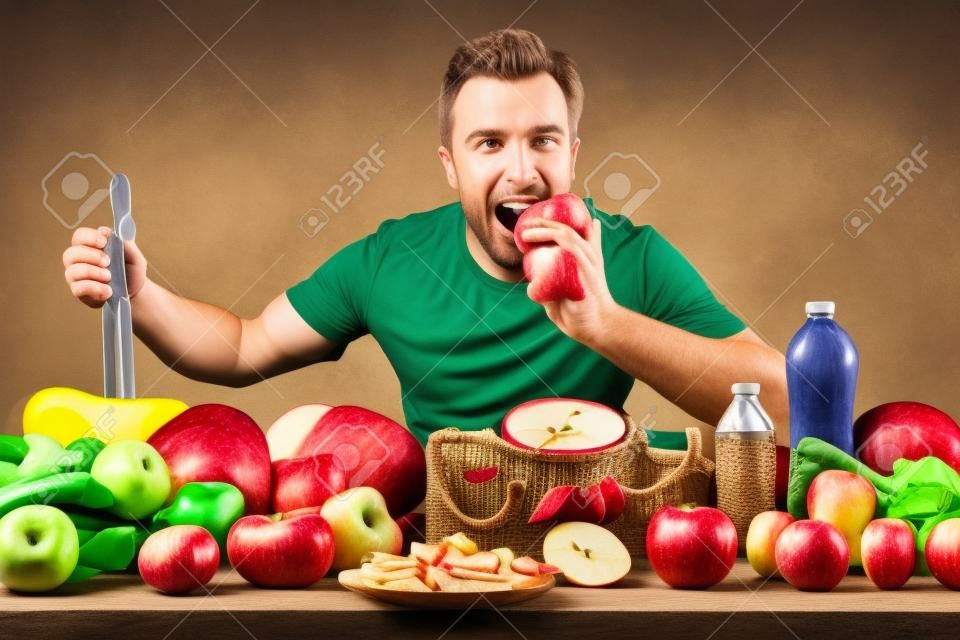 Sportler, der Apfel isst und Obst und Gemüse, Waagen und Zubehör für den Sport auf einem Tisch mit venezianischem Hintergrund zeigt.