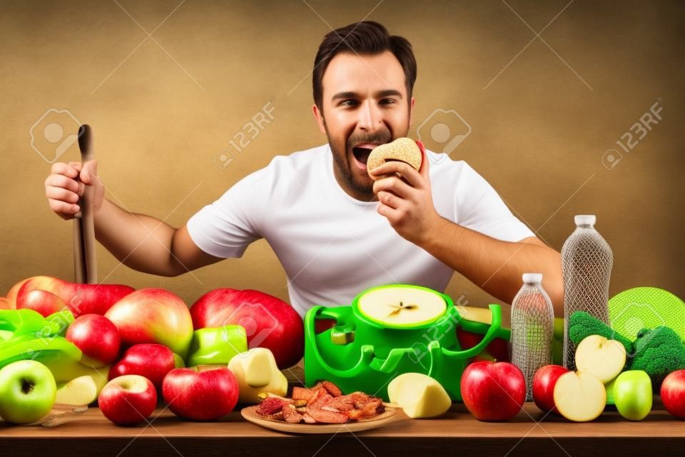 Deportista comiendo manzana mostrando frutas y verduras, escamas y accesorios para deportes en una mesa con fondo veneciano.