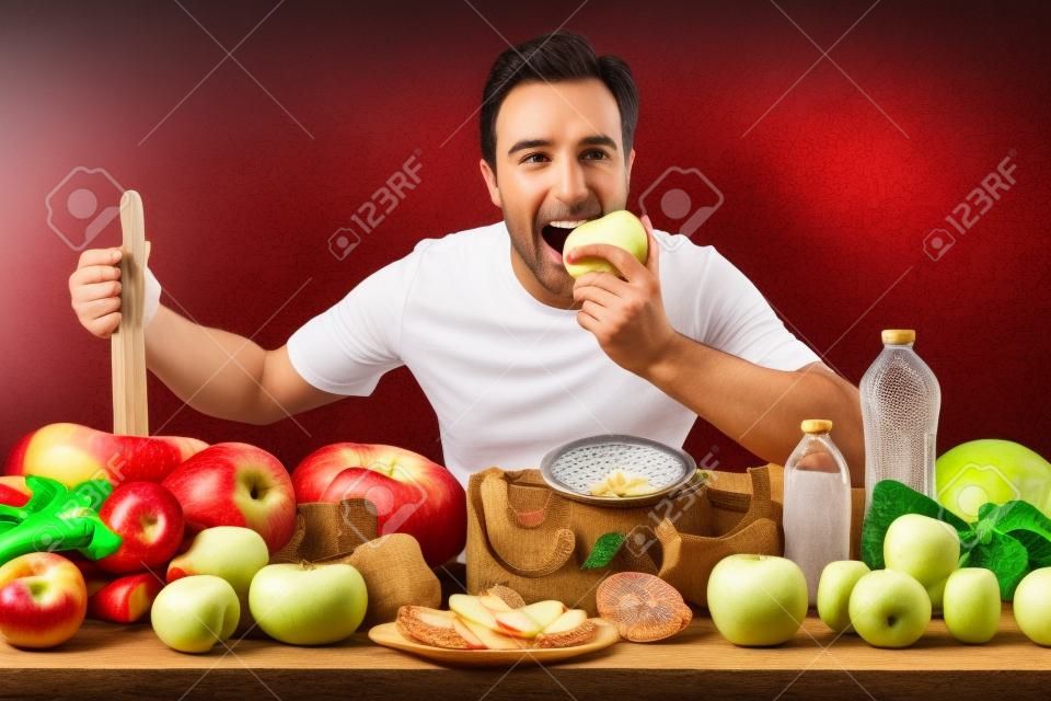 Sportivo che mangia mela che mostra frutta e verdura, bilance e accessori per lo sport su un tavolo con sfondo veneziano.