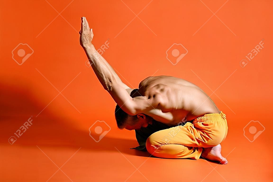 Alter Mann, der Yoga praktiziert und Dehnübungen vor orangefarbenem Hintergrund macht
