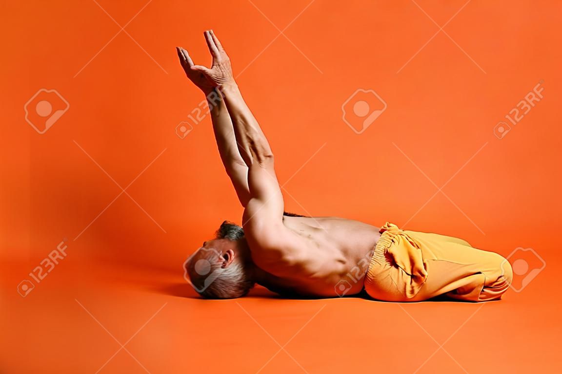 Alter Mann, der Yoga praktiziert und Dehnübungen vor orangefarbenem Hintergrund macht