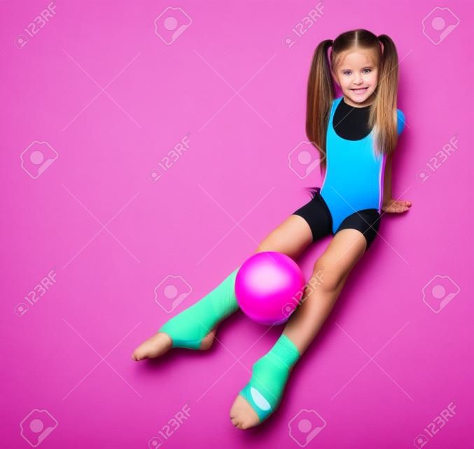Cute girl gymnast with long hair in black sport body and uppers sitting on floor holding pink gymnastic ball between legs over white background, top view. Rhytmhic gimnastics beauty cocnept