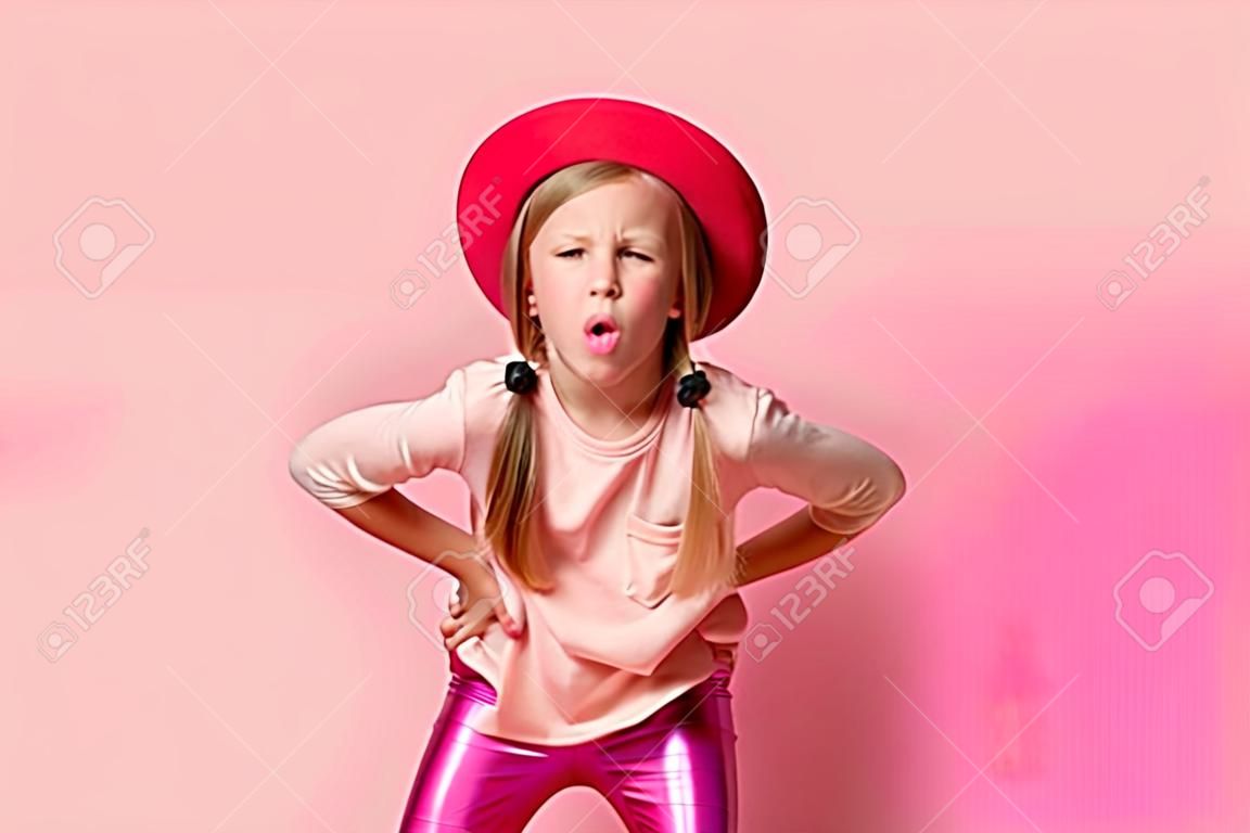 Mischievous little girl leaning forward with hands on hips and lolling while teasing or trolling someone. Close up shot isolated on pink. Stylish kids, childhood, emotions and gestures, games