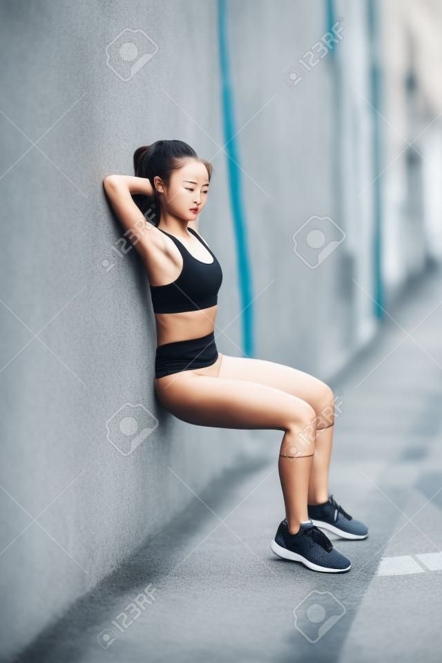 年轻时尚的女运动员是伸展在街上一个夏季的一天，她是很柔韧灵活，由于她穿着时髦的运动装运动鞋的定期培训