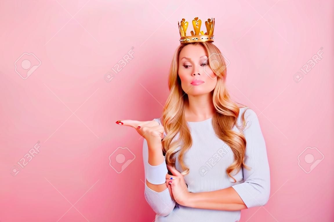 Porträt mit Copyspace leerer Ort der selbstbewussten stolzen arroganten Frau mit goldener Krone auf ihrem Kopf, Zeigefinger zeigend, Fräulein ich will, lokalisiert auf rosa Hintergrund