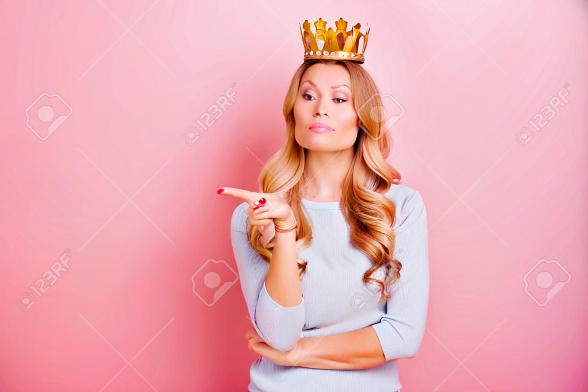 Portrait with copyspace empty place of confident proud arrogant woman with gold crown on her head pointing forefinger, miss I want, isolated on pink background