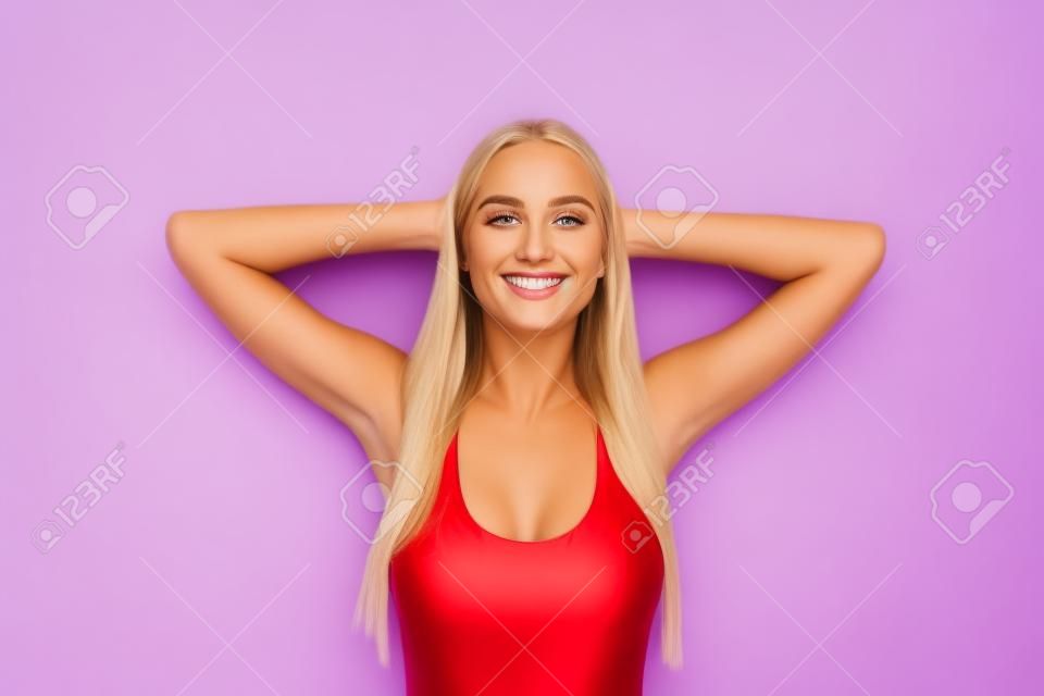 Portret młodej atrakcyjnej ładnej wspaniałej blondynki uśmiechnięta dziewczyna z prostymi włosami na sobie czerwony strój kąpielowy, zrelaksowany, odpoczywając na wakacyjnej wycieczce. Pojedynczo na fioletowym tle