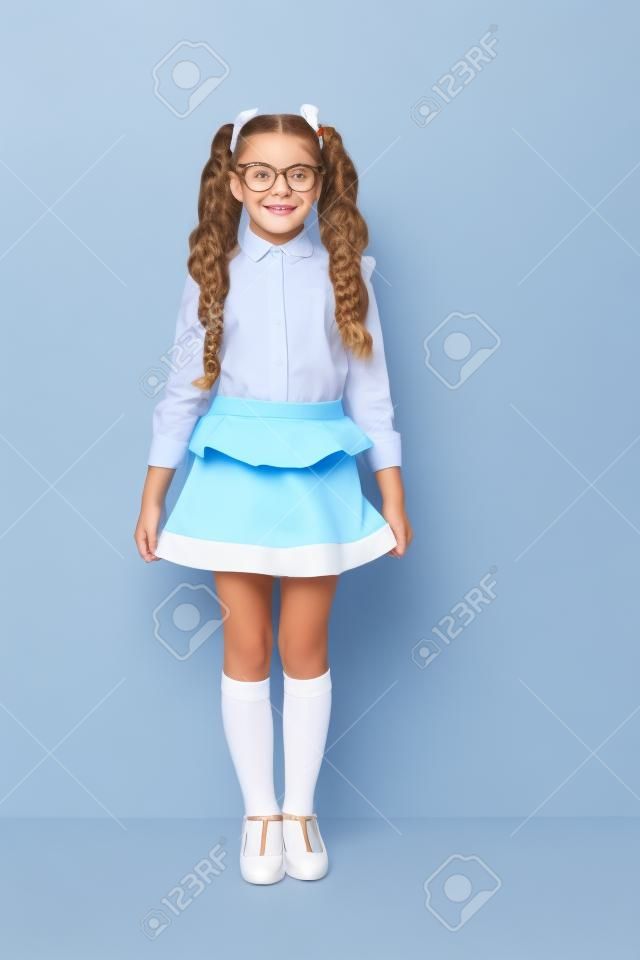 В полный рост милая милая жизнерадостная очаровательная милая стильная маленькая девочка с вьющимися хвостиками в белой формальной блузке, короткой синей юбке. Изолированные на сером фоне