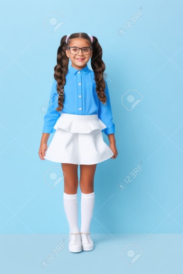 Full body size length of nice cute cheerful adorable lovely stylish little small girl with curly ponytails in white formal blouse shirt, short blue skirt. Isolated over grey background