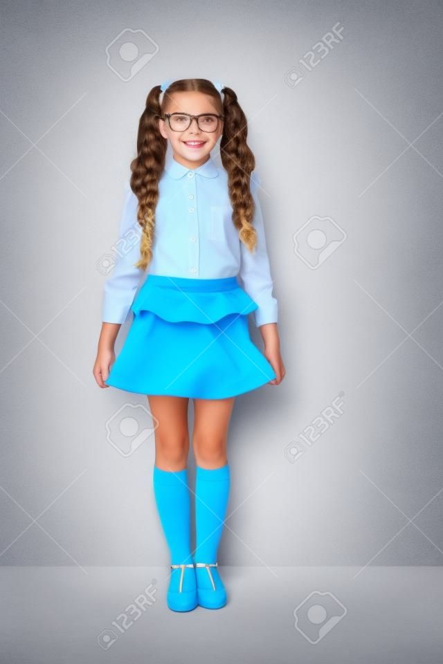 Full body size length of nice cute cheerful adorable lovely stylish little small girl with curly ponytails in white formal blouse shirt, short blue skirt. Isolated over grey background