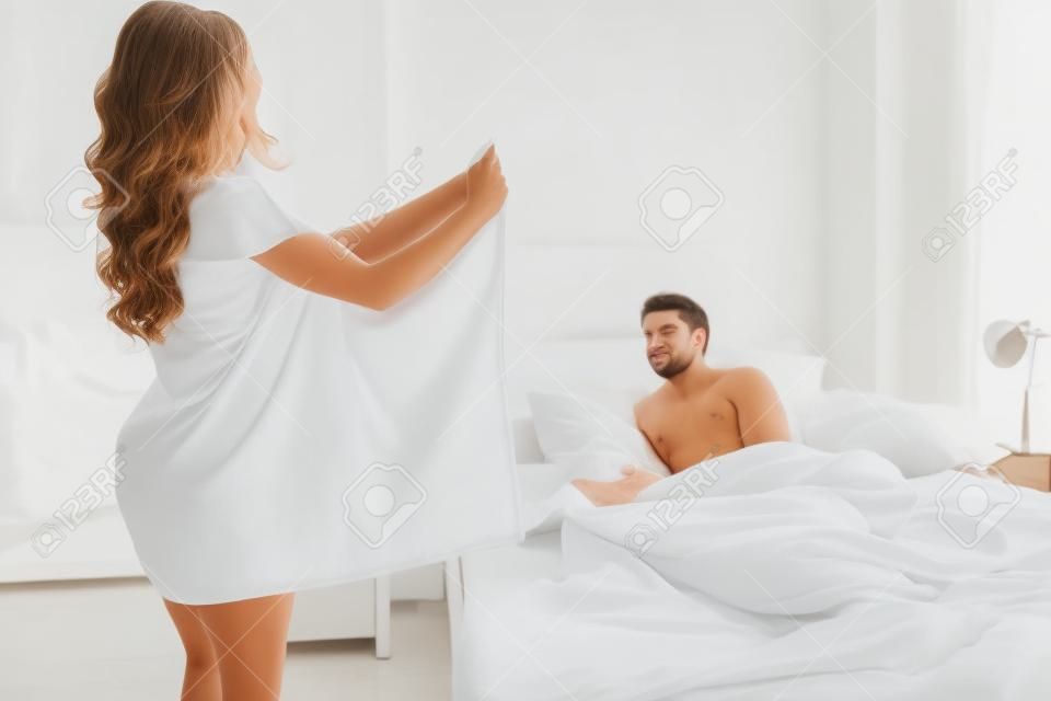 Una donna con un asciugamano bianco mostra il suo corpo al marito sdraiato sul letto. vista laterale