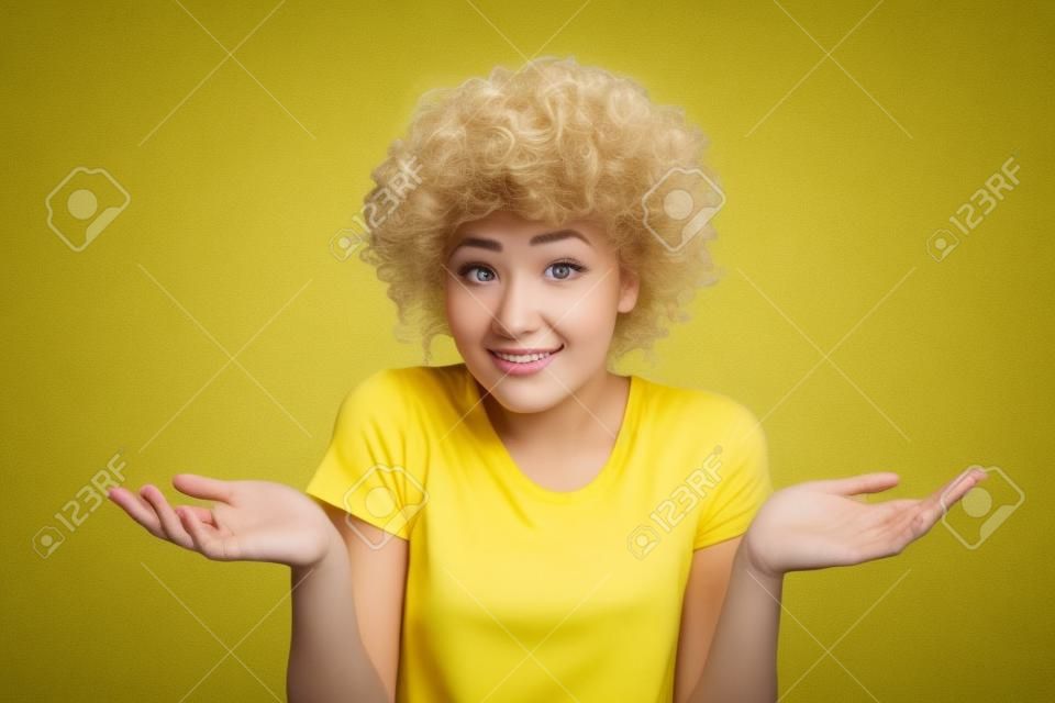 Retrato de primer plano de ella ella agradable atractiva desconcertada ignorante chica de pelo ondulado mostrando gesto sin información aislada sobre fondo amarillo brillante brillante
