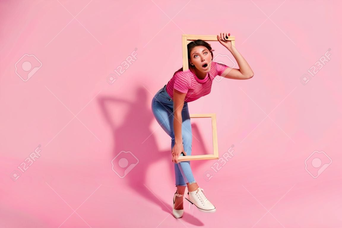 분홍색 배경에 고립된 삶의 경계선을 벗어나려고 하는 캐주얼한 줄무늬 티셔츠 청바지를 입은 그녀의 전체 길이 신체 크기 보기