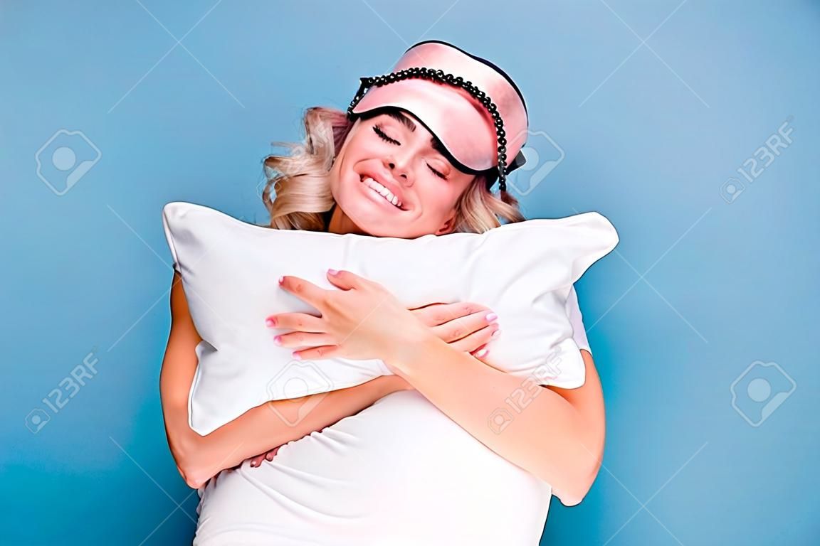Close up photo beautiful funky her she lady white teeth hands arms palms hold cuddle big large pillow glad day off wear sleeping pink mask casual white t-shirt clothes isolated blue background