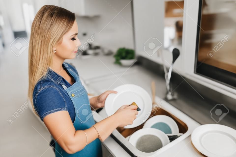 Close up side profile photo attentive beautiful she her lady cleaner bright kitchen hold dirty plate spring cleanup preparing meeting holiday gathering wear casual jeans denim shirt apron flat indoors