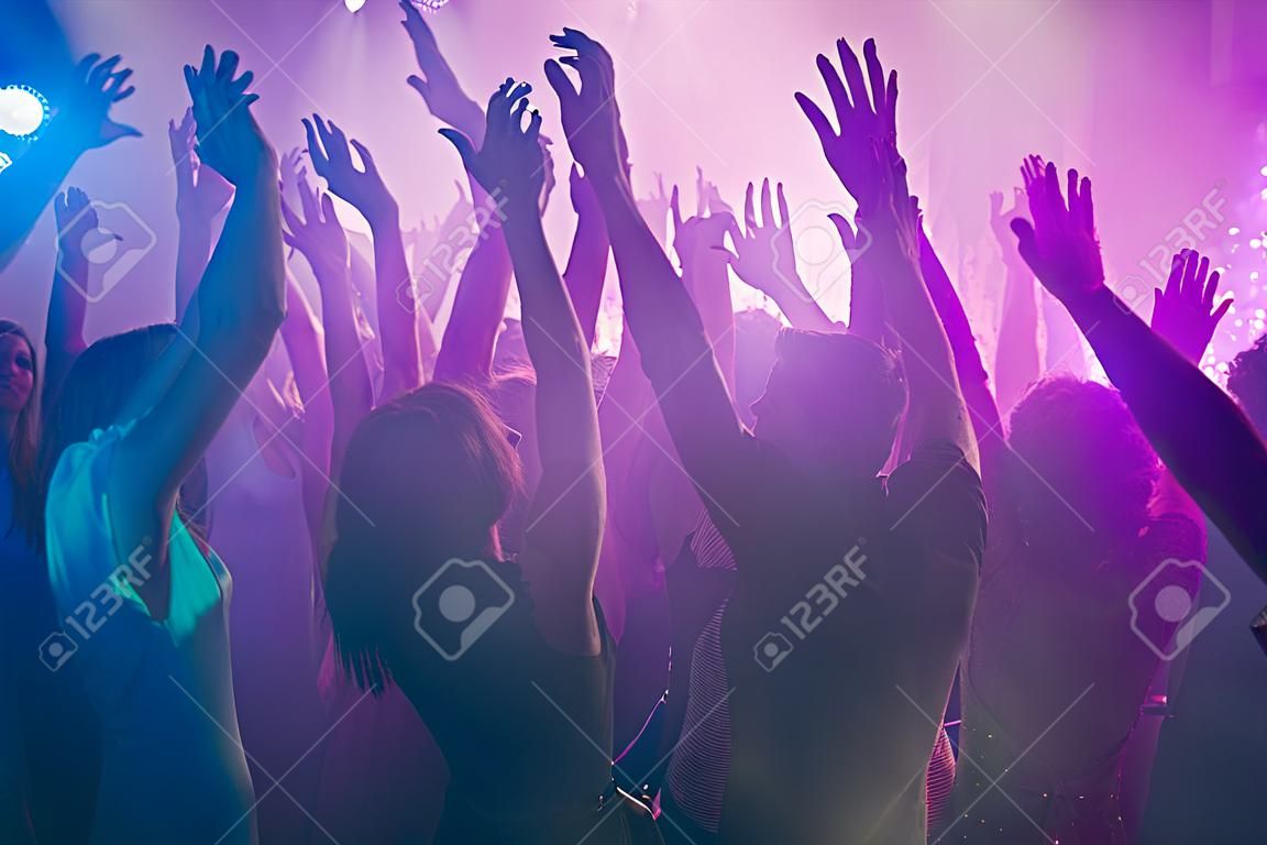 Close up photo of many birthday party people dancing clubbing purple lights confetti fog nightclub hands raised shiny formal-wear
