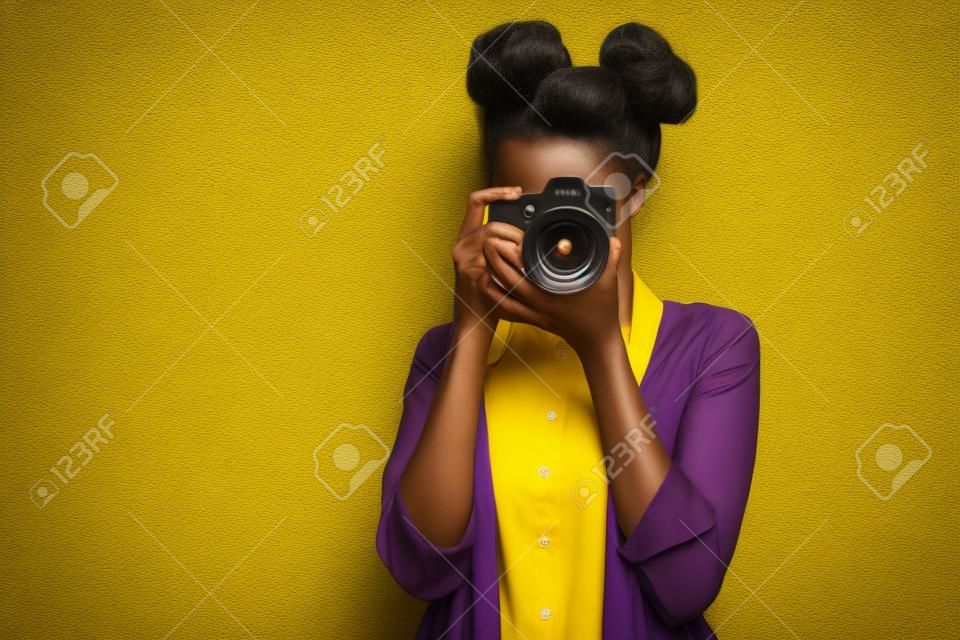 Foto di una straordinaria signora dalla pelle scura che tiene una foto digicam nelle mani che fotografa, visite turistiche straniere all'estero indossano pantaloni della camicia gialla isolati sullo sfondo di colore viola