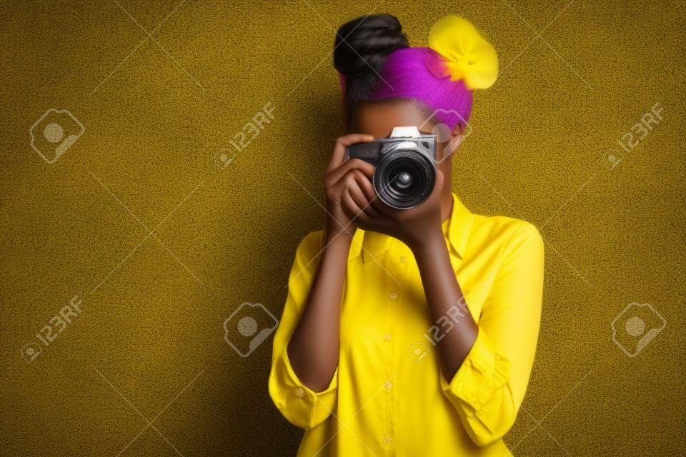 Foto de una increíble dama de piel oscura con cámara fotográfica fotográfica en las manos fotografiando, turismo extranjero en el extranjero, use pantalones de camisa amarilla aislados de fondo de color púrpura