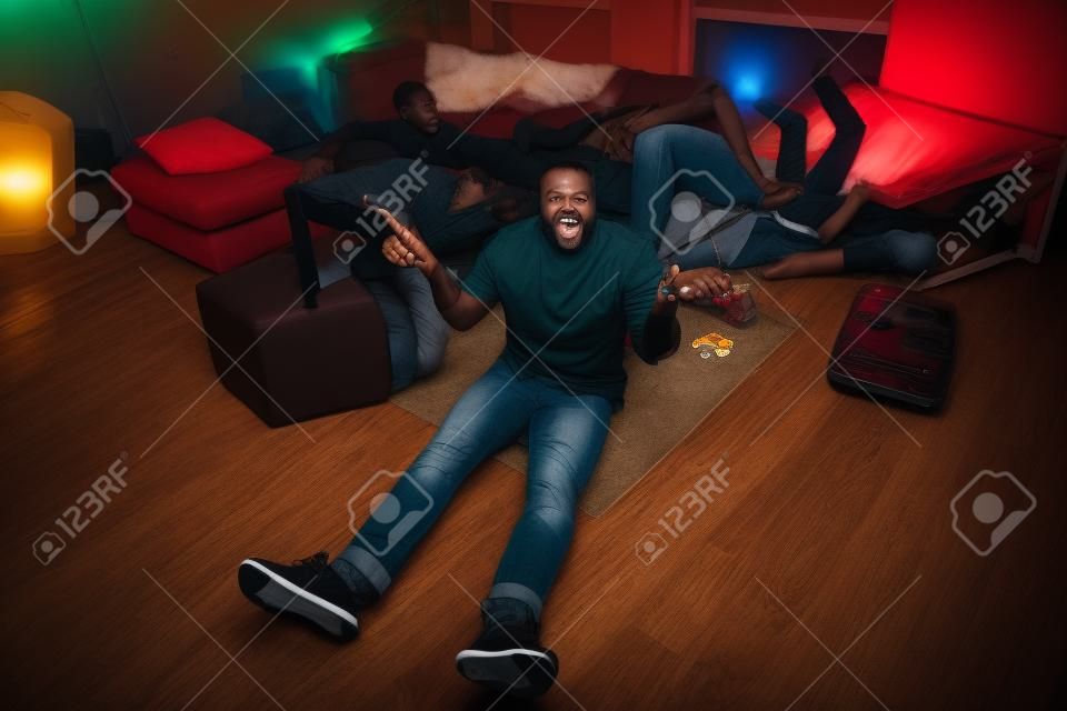 Boven boven hoge hoek uitzicht volledige lichaam foto van afro-Amerikaanse kerel zitten vloer houden lege bier fles ophaal schouders hebben overhandigen zijn vrienden slapen in huis binnen