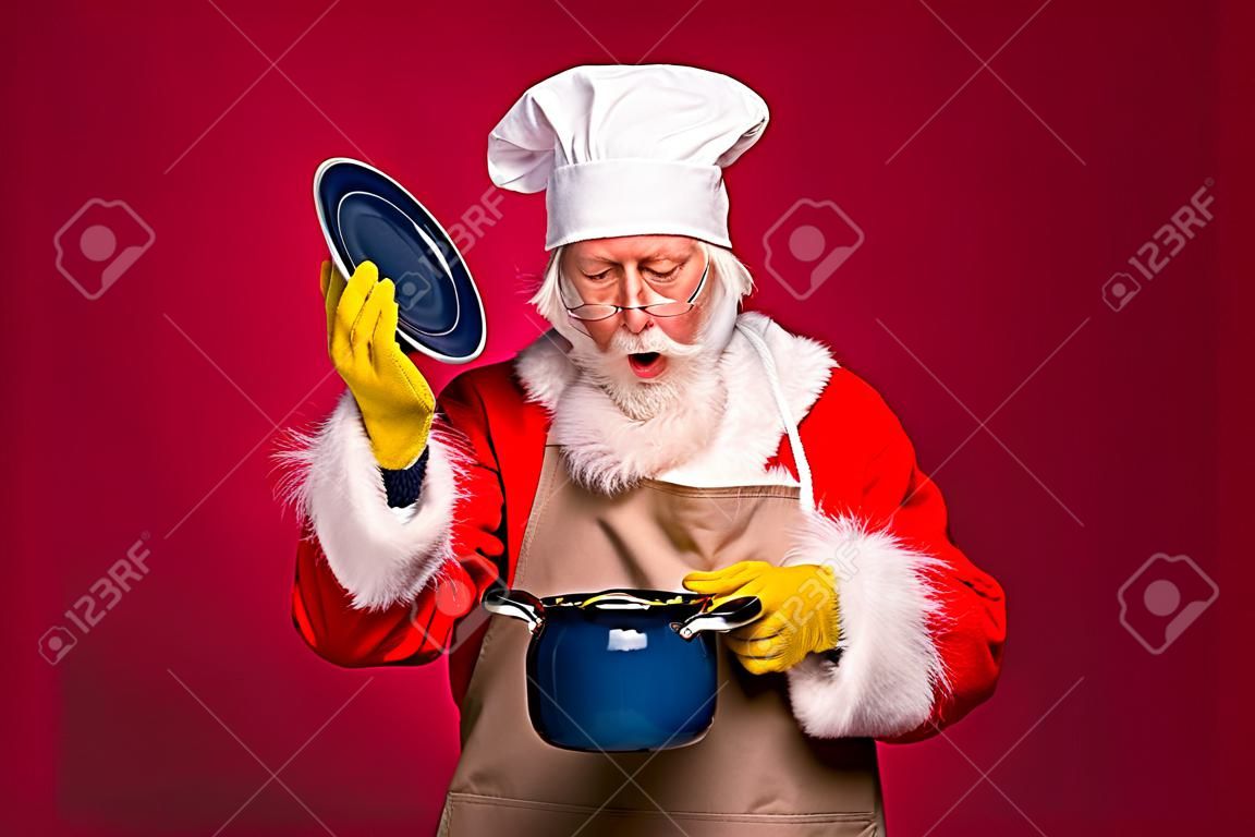 Zdjęcie zdumionego świętego mikołaja otwórz pokrywę garnka rondel x-mas rozgotowany obiad nosić cahef czapka czerwony fartuch odizolowany jasny połysk kolor tła