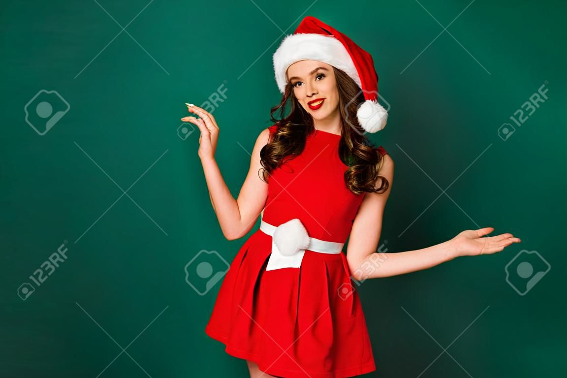 La foto di una magnifica ragazza affascinante e chic gode di un evento miracoloso di Natale, indossa un bel look da Babbo Natale, un copricapo isolato su uno sfondo di colore verde