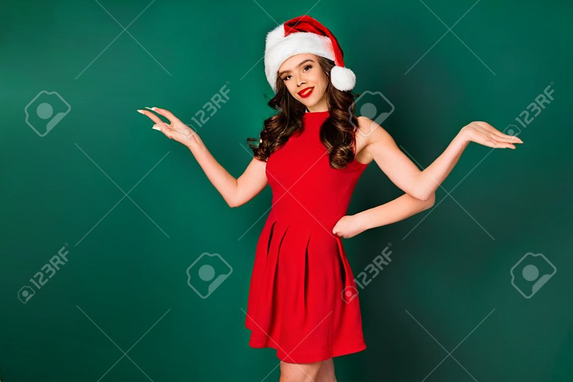 La foto di una magnifica ragazza affascinante e chic gode di un evento miracoloso di Natale, indossa un bel look da Babbo Natale, un copricapo isolato su uno sfondo di colore verde