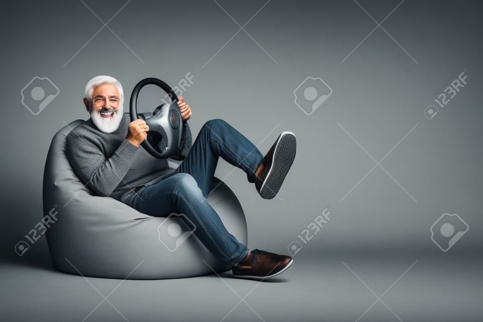 Portrait d'un homme barbu aux cheveux gris assis dans une chaise de sac s'amusant tenant le volant
