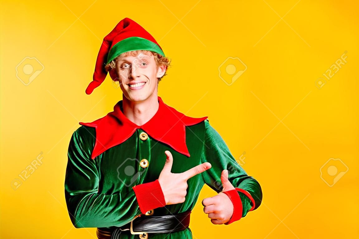 Portrait de son elfe de gars drôle joyeux attrayant heureux joyeux gai démontrant l'espace de copie Eve Noel annonce des conseils publicitaires isolés sur fond de couleur jaune vif brillant brillant
