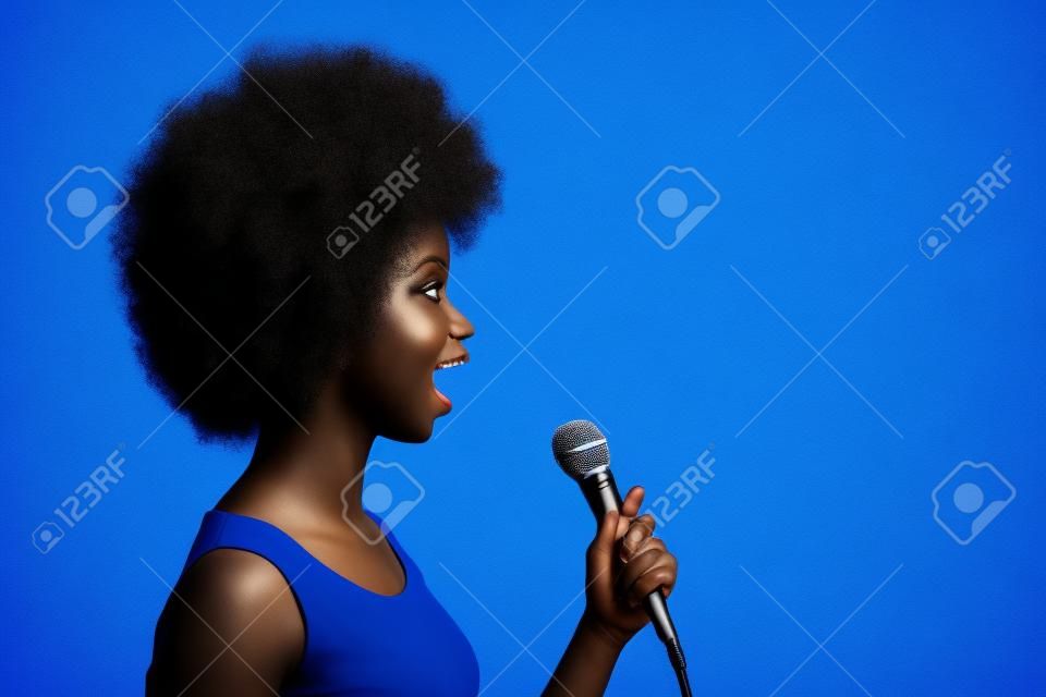 Photo side profile portrait of pretty black skinned girl singing on microphone looking at copyspace isolated on bright blue color background