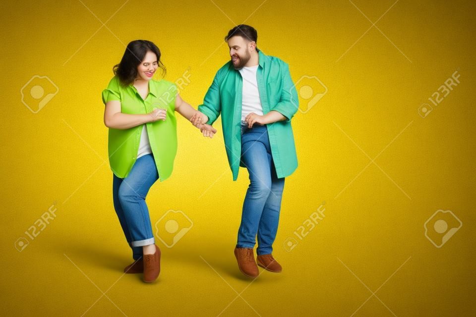 Foto des süßen, entzückenden Ehemanns, der Jeanshemden trägt, die leeren Raum tanzen, isolierter gelber Farbhintergrund