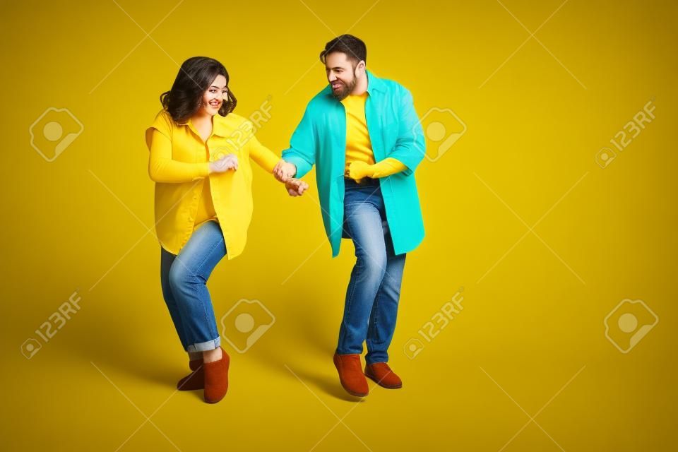 Foto des süßen, entzückenden Ehemanns, der Jeanshemden trägt, die leeren Raum tanzen, isolierter gelber Farbhintergrund