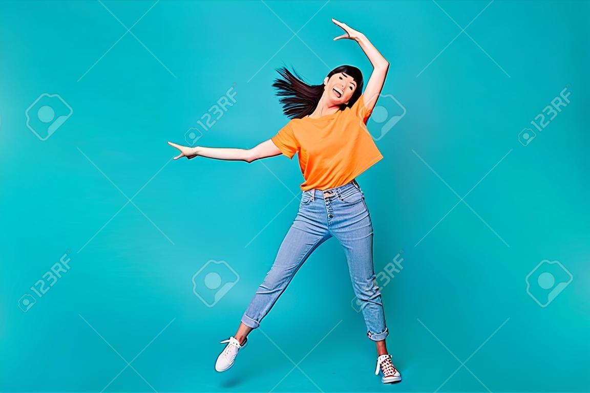 Foto in Originalgröße einer hübschen brünetten Dame in Tanzkleidung, T-Shirt, Jeansstiefeln, isoliert auf türkisfarbenem Hintergrund