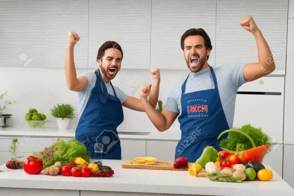 Portret van twee verheugde overjoyed partners verhogen vuisten op vieren succes bereiken keuken binnen