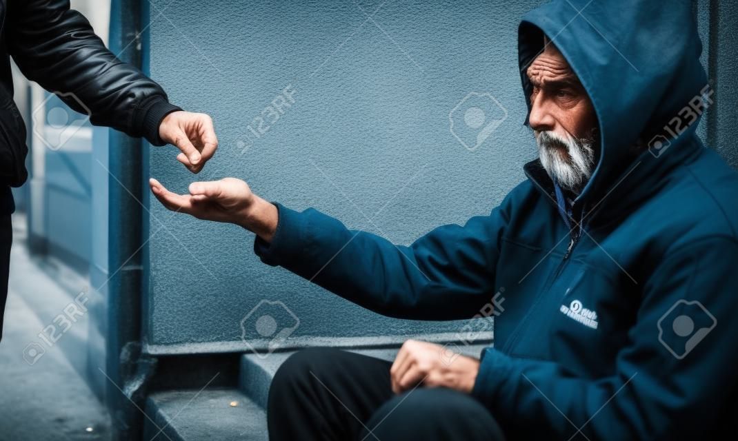 Homem sem-teto esfomeado sentado na rua da cidade à espera de ajuda e dinheiro.