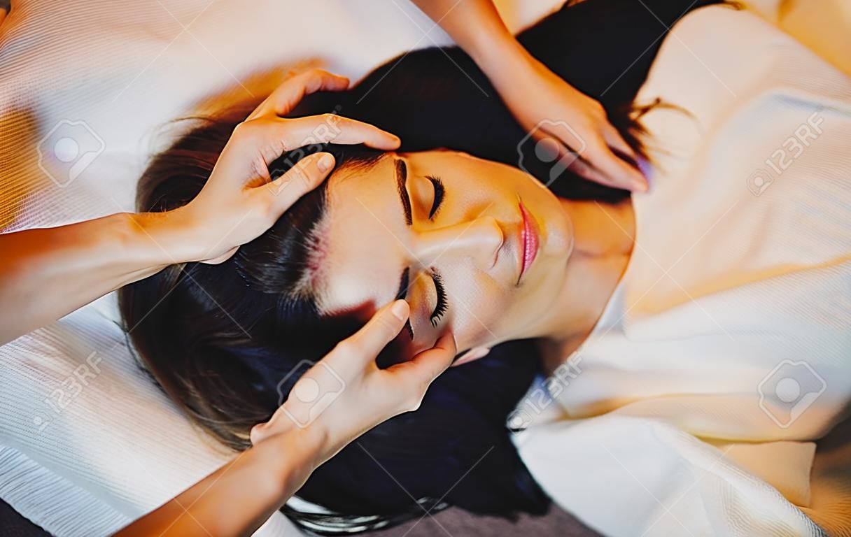 Ritratto di vista superiore di una donna caucasica bruna sdraiata sul divano mentre ha una sessione di massaggio alla testa