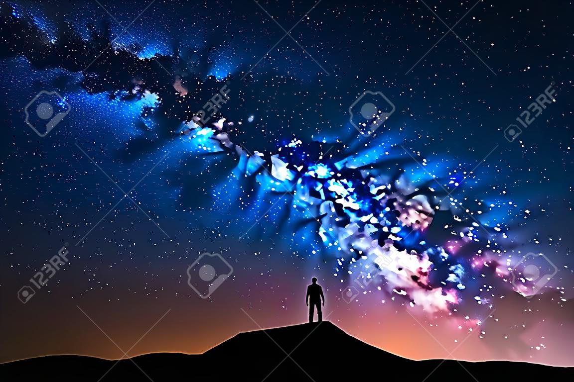 Via Láctea. Belo céu noturno com estrelas e silhueta de um homem sozinho na montanha. Maneira leitosa azul com luz vermelha e homem na colina. Fundo com galáxia e silhueta de um homem. Universo