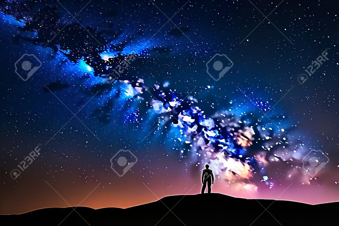 Via Láctea. Belo céu noturno com estrelas e silhueta de um homem sozinho na montanha. Maneira leitosa azul com luz vermelha e homem na colina. Fundo com galáxia e silhueta de um homem. Universo