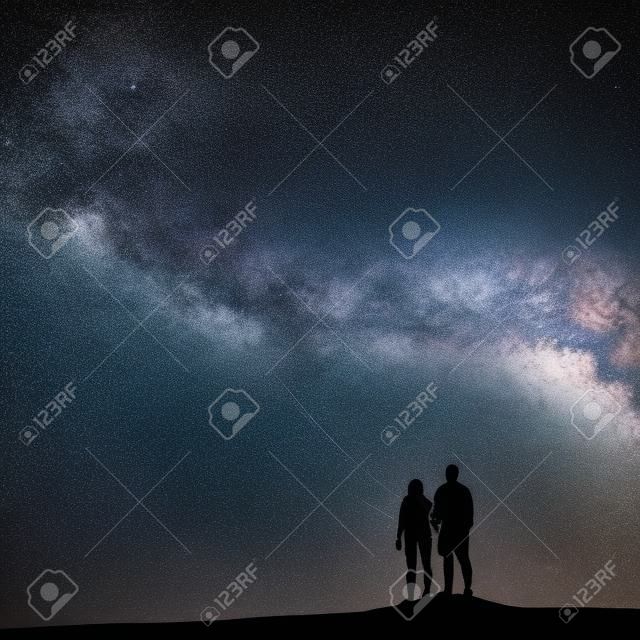 Milchstraße mit Menschen auf dem Berg. Landschaft mit Nachthimmel mit Sternen und Silhouette von stehenden Mann und Frau. Milchstraße mit Paar Reisende gegen schöne Galaxie. Universum