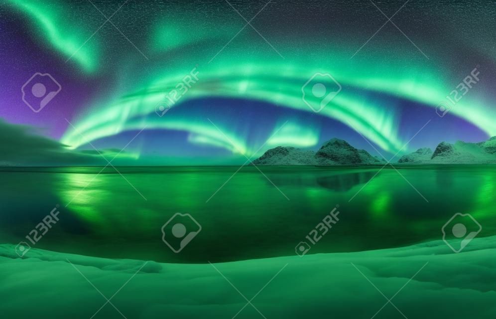 Aurora. Lofoten adalarında kuzey ışıkları, Norveç. Kutup ışıkları ile yıldızlı mavi gökyüzü. Aurora ile gece kış manzarası, gökyüzü yansıması ile deniz, plaj, dağlar, şehir ışıkları. Yeşil aurora borealis