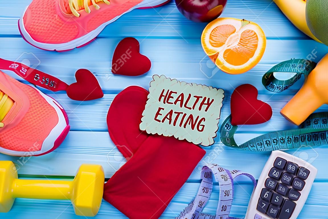 Gezond eten, diëten, afslanken en gewichtsverlies concept. Dumbells, sneakers, fruit, meettape, rekenmachine en stof hart. Gezondheid en fitness.