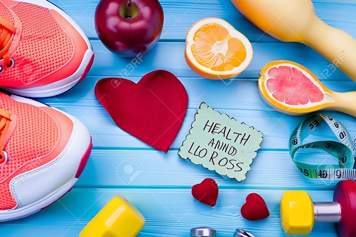 Healthy eating, dieting, slimming and weight loss concept. Dumbbells, sneakers, fruits, measuring tape, calculator and fabric heart. Health and fitness.