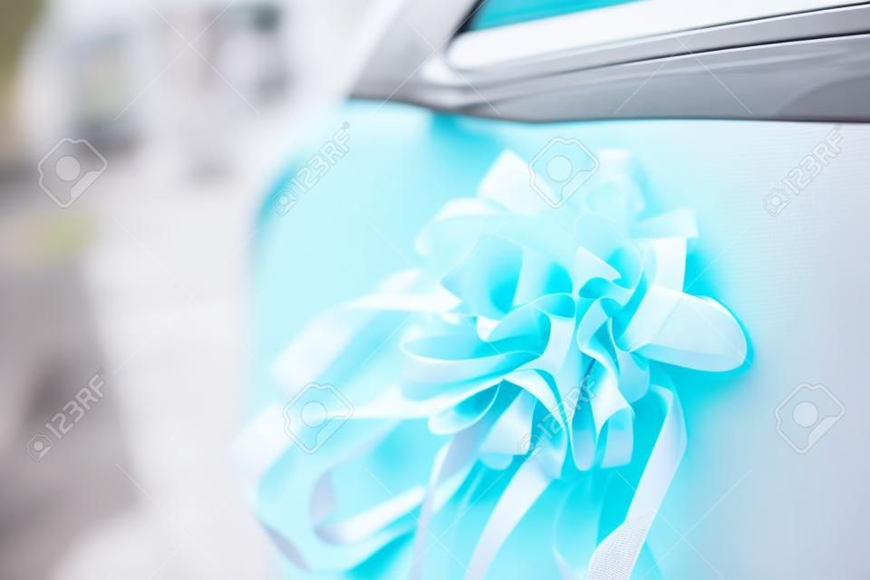 Bouquet artificiel avec des rubans attachés à la porte d'une voiture blanche. Décoration sur la porte de la voiture le jour du mariage. Services d'organisation d'événements solennels et mémorables.