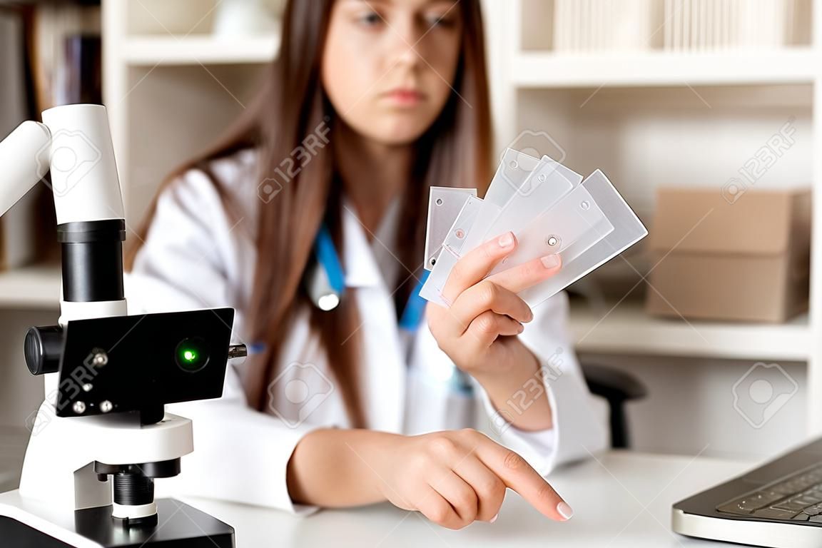 Joven doctora o científica que usa microscopio, tiene una llamada en línea que muestra muestras, enseña en línea