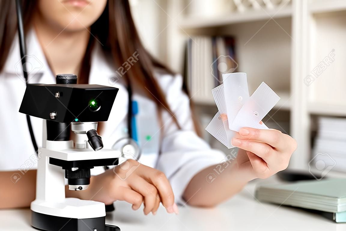 Joven doctora o científica que usa microscopio, tiene una llamada en línea que muestra muestras, enseña en línea