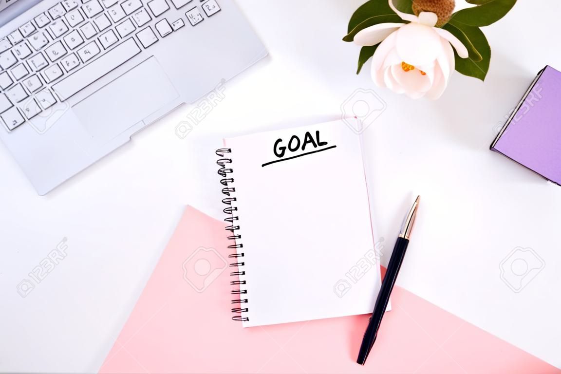 Schreiben Sie ein Ziel für das neue Jahr 2010 in ein weißes Notizbuch auf einem weißen Desktop neben einer Kaffeetasse und einer Tastatur. Draufsicht, flaches Layout