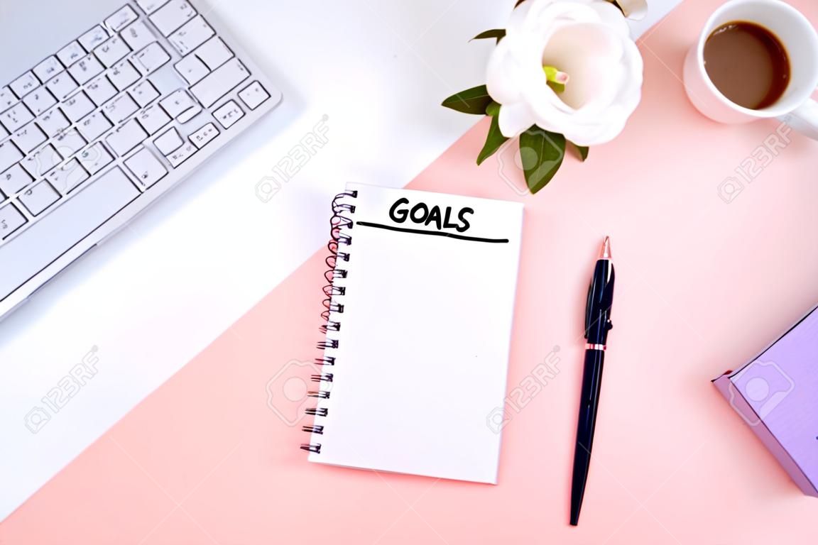 Write a goal for the new year 2010 in a white notebook on a white desktop next to a coffee mug and a keyboard. Top view, flat layout