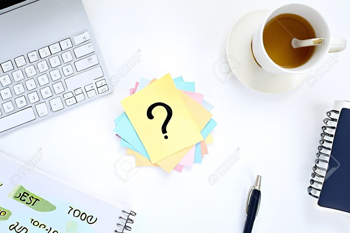 Mehrfarbige Aufkleber mit Fragezeichen auf weißem Desktop neben einer Tasse Kaffee und einer Tastatur