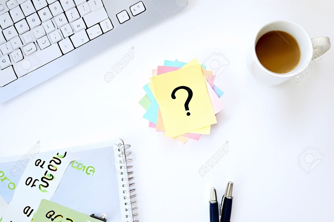 Mehrfarbige Aufkleber mit Fragezeichen auf weißem Desktop neben einer Tasse Kaffee und einer Tastatur