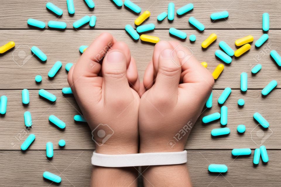 A Pill Abuse Concept With 2 Tied Hands Surrounded By Many Pills On A Wooden Table