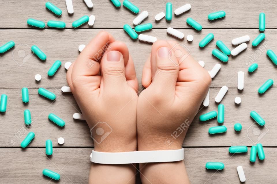 A Pill Abuse Concept With 2 Tied Hands Surrounded By Many Pills On A Wooden Table
